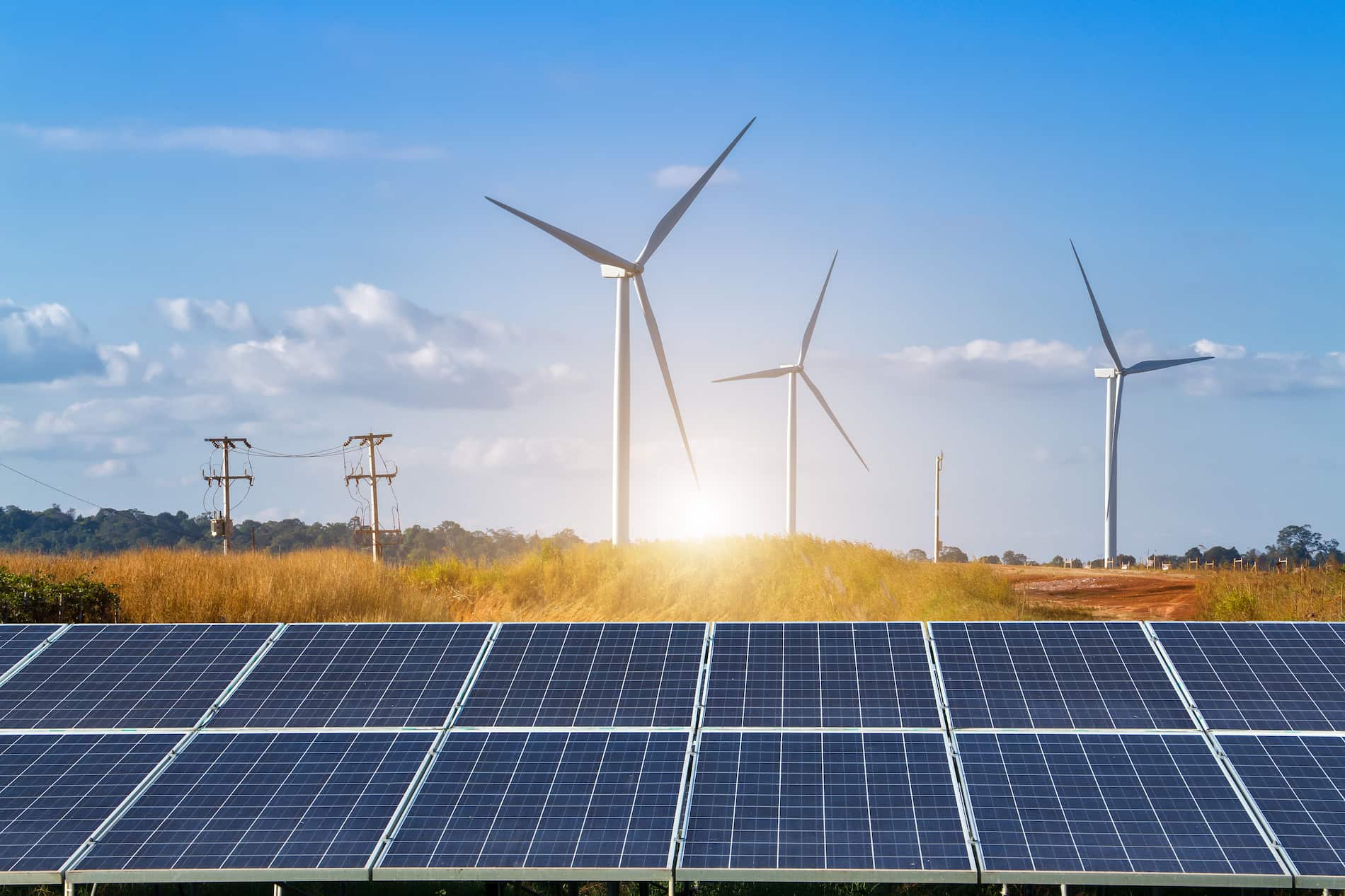 Windmills and solar panels with sun in background.