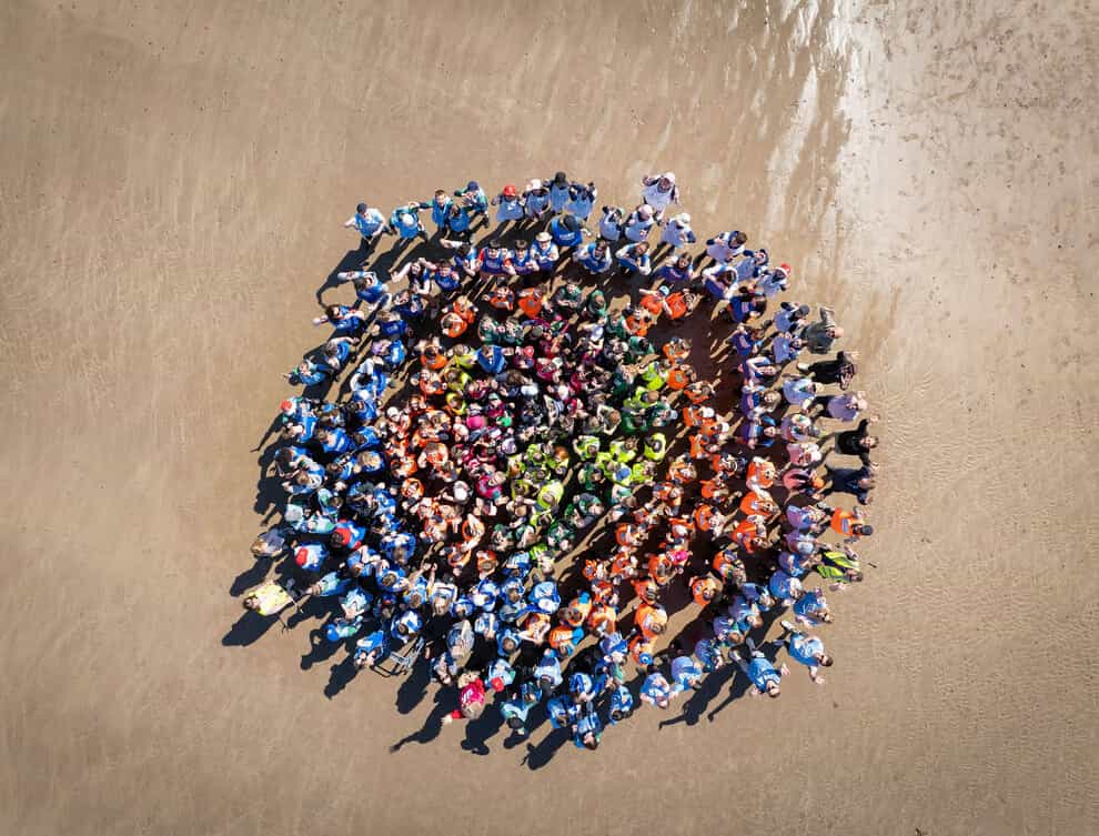 Circle of people in colourful clothing on beach.